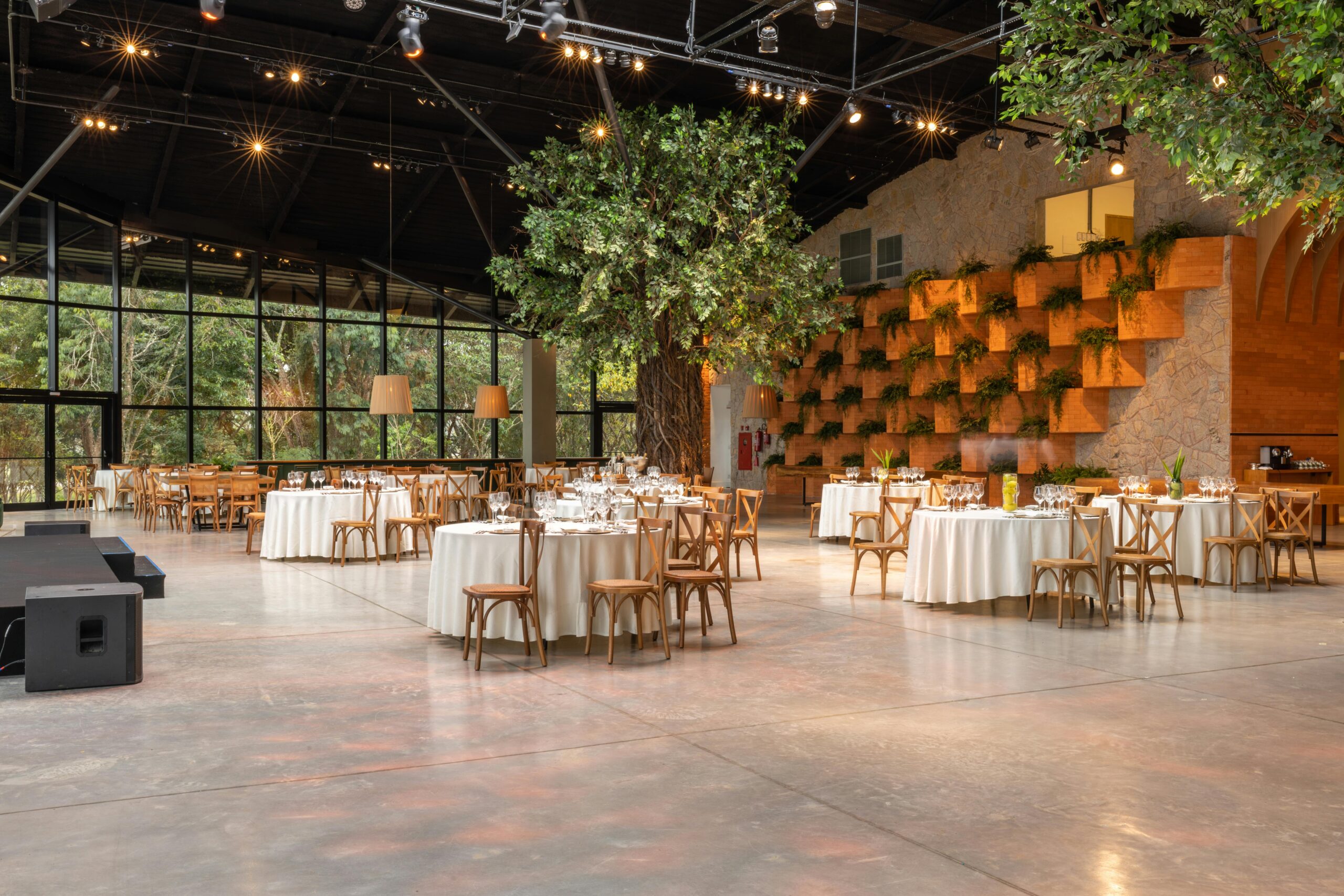 Luxurious banquet hall with round tables set for dining and lush indoor trees for a modern ambiance.