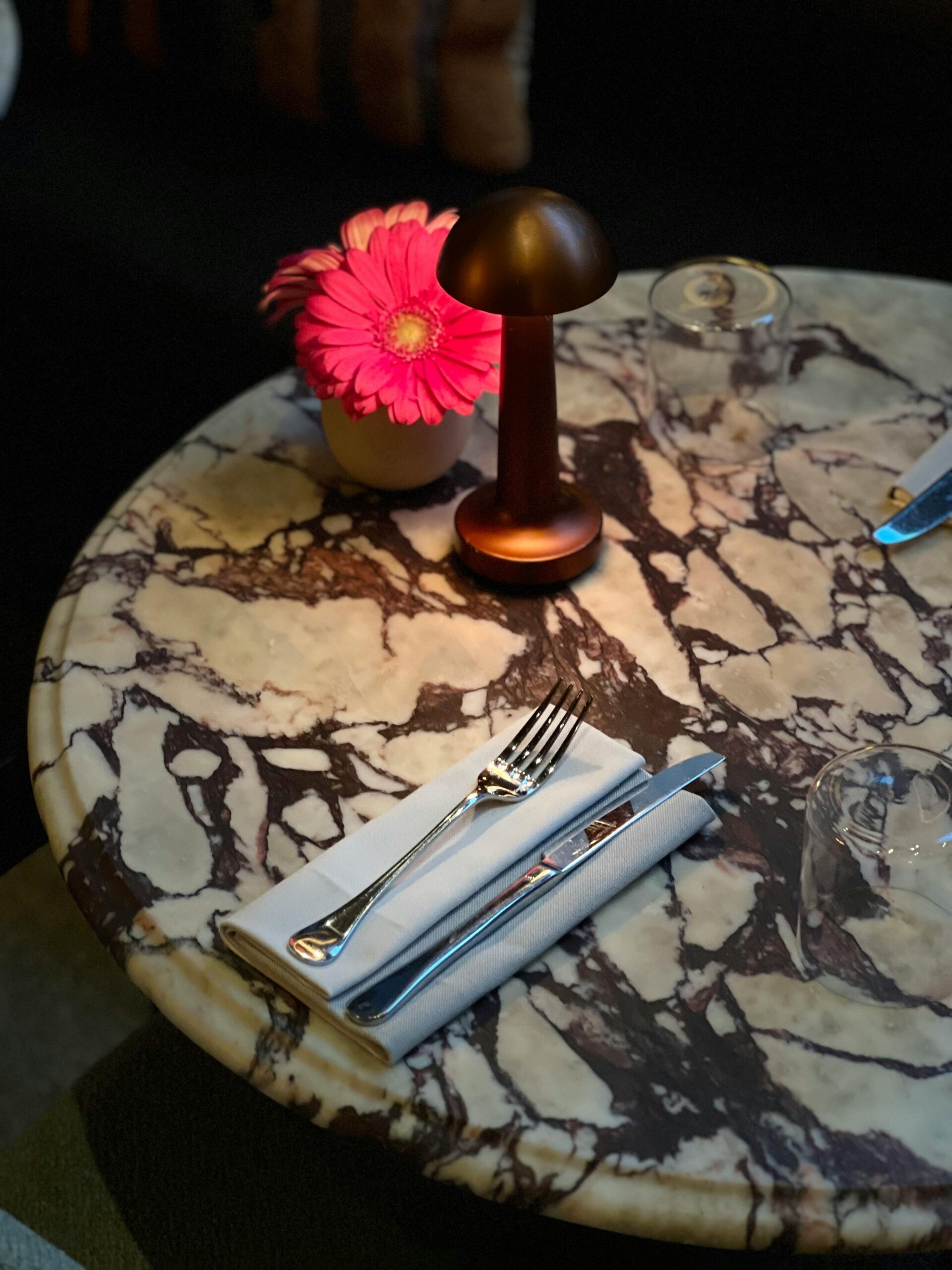 Stylish marble table at a restaurant with pink gerbera and lamp.