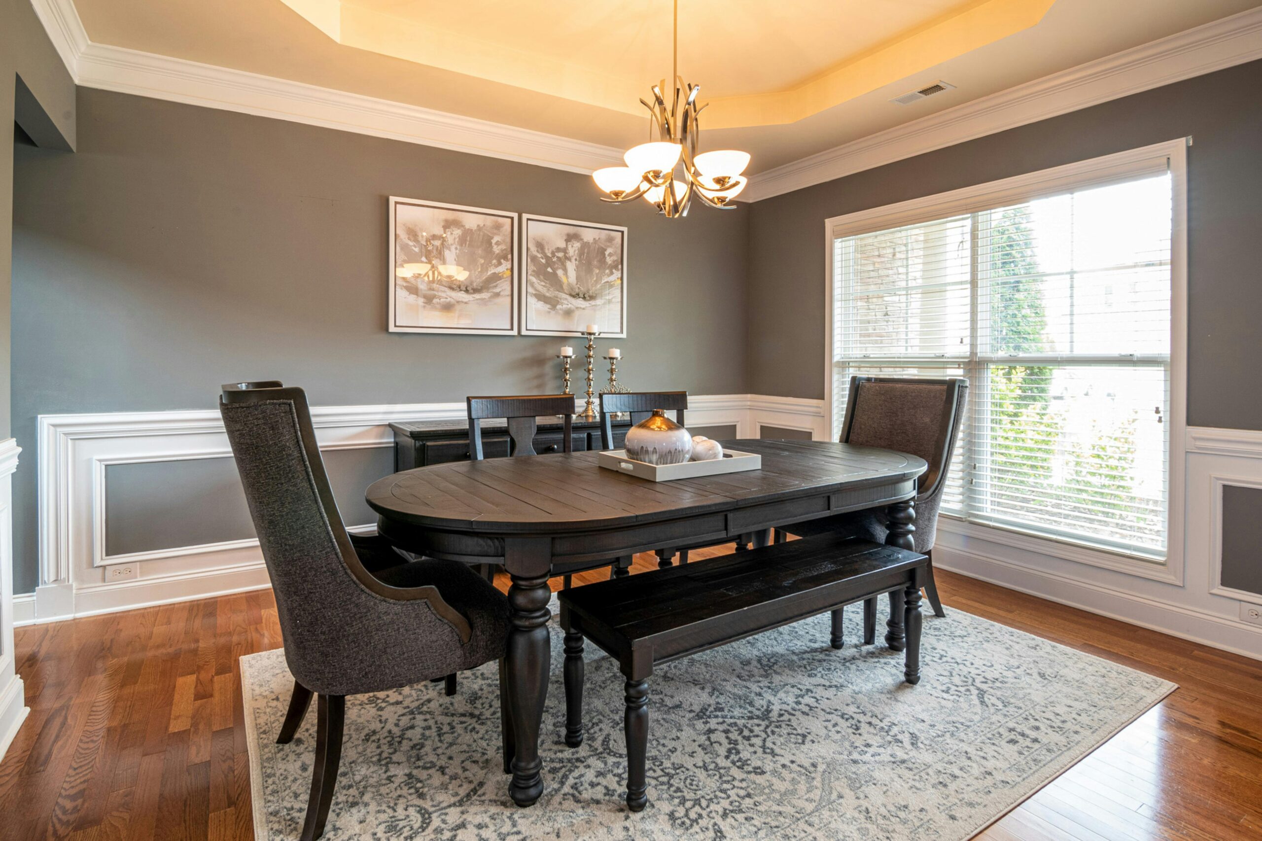 Chic modern dining room featuring dark wooden furniture, a chandelier, and large windows.